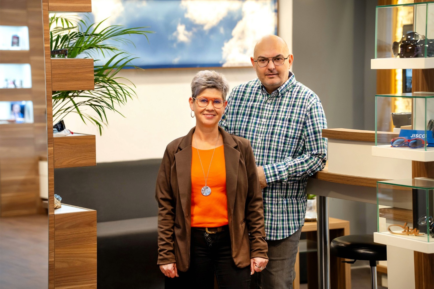 Zwei lächelnde Erwachsene in moderner Optik, sie trägt orangefarbene Kleidung